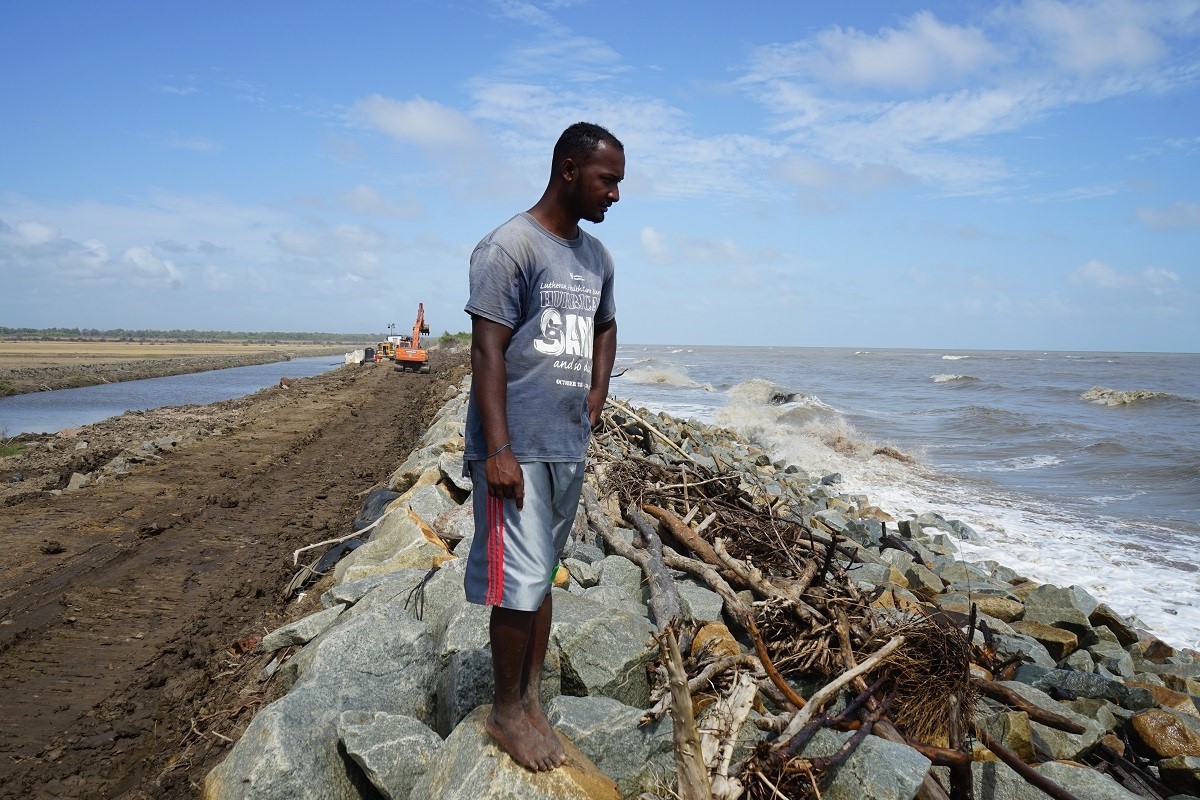 Richard Jardim, Reisbauer, blickt auf die Meeresbrandung am Deich an der Küste Guyanas. Der Klimawandel lässt den Meeresspiegel steigen und bedroht die dahinter liegenden Felder. Foto: Sandra Weiss